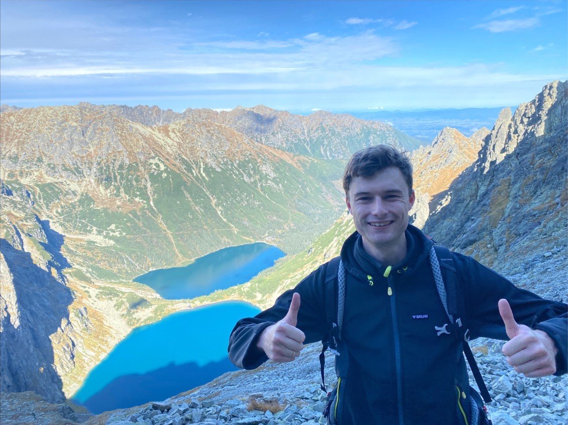 Paul Smuts, creator of the Paul in Poland travel blog hiking in the Tatra Mountains with Morskie Oko and Czarny Staw lakes in the background on the route to Rysy Mountain.