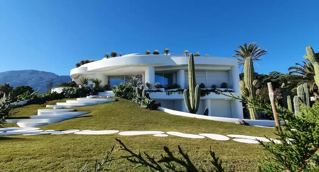 Contemporary white villa with garden and cacti in Dénia, Spain under a clear blue sky.