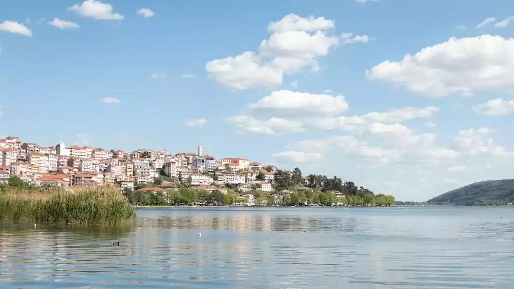 Scenic view of Kastoria's lakeside cityscape with a serene lake and blue sky.