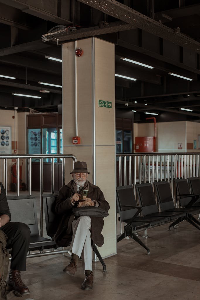 An elderly man dressed warmly sitting in an Istanbul train station, reading a book.