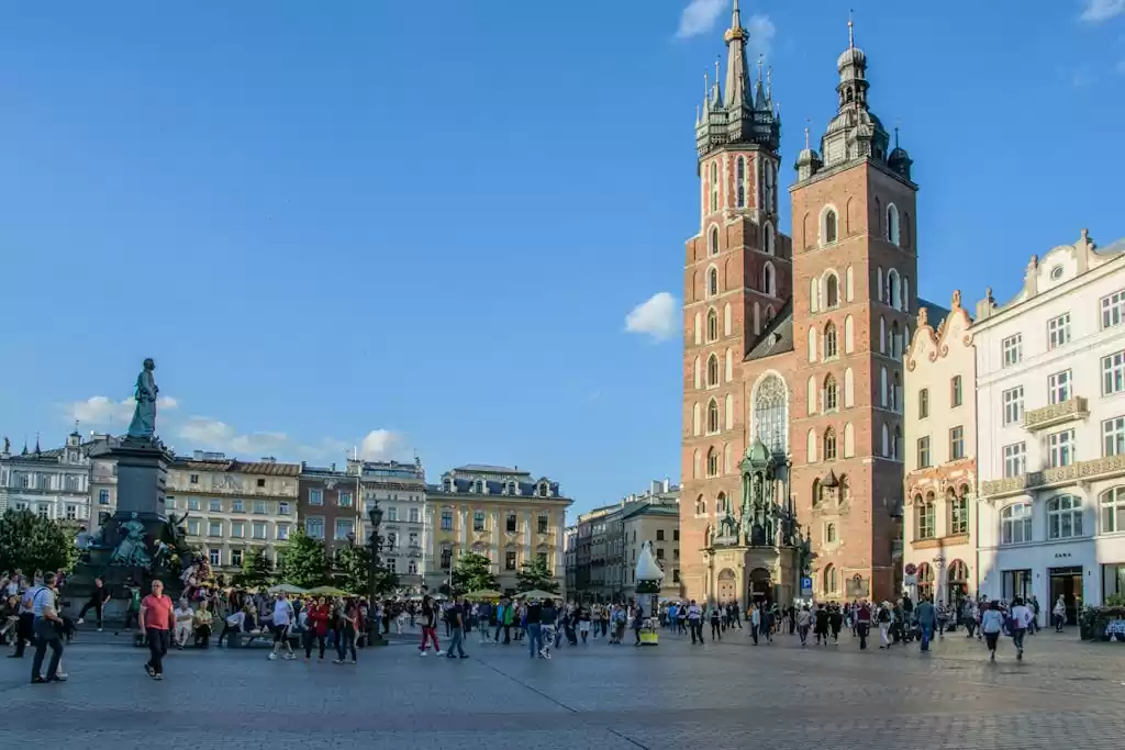 Sunny day at Main Market Square in Kraków, featuring St. Mary's Basilica and lively crowd.