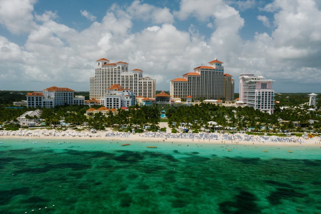 Aerial view of a vibrant resort beach, turquoise sea, and lush trees under a cloudy sky.