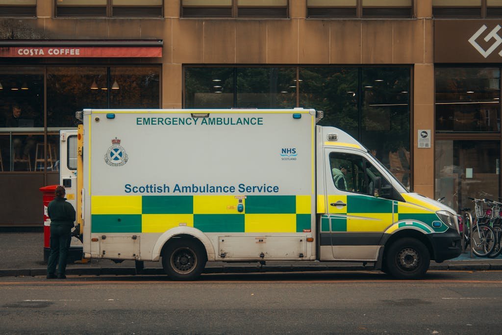 Scottish Ambulance Service vehicle parked on a city street with a pedestrian nearby.