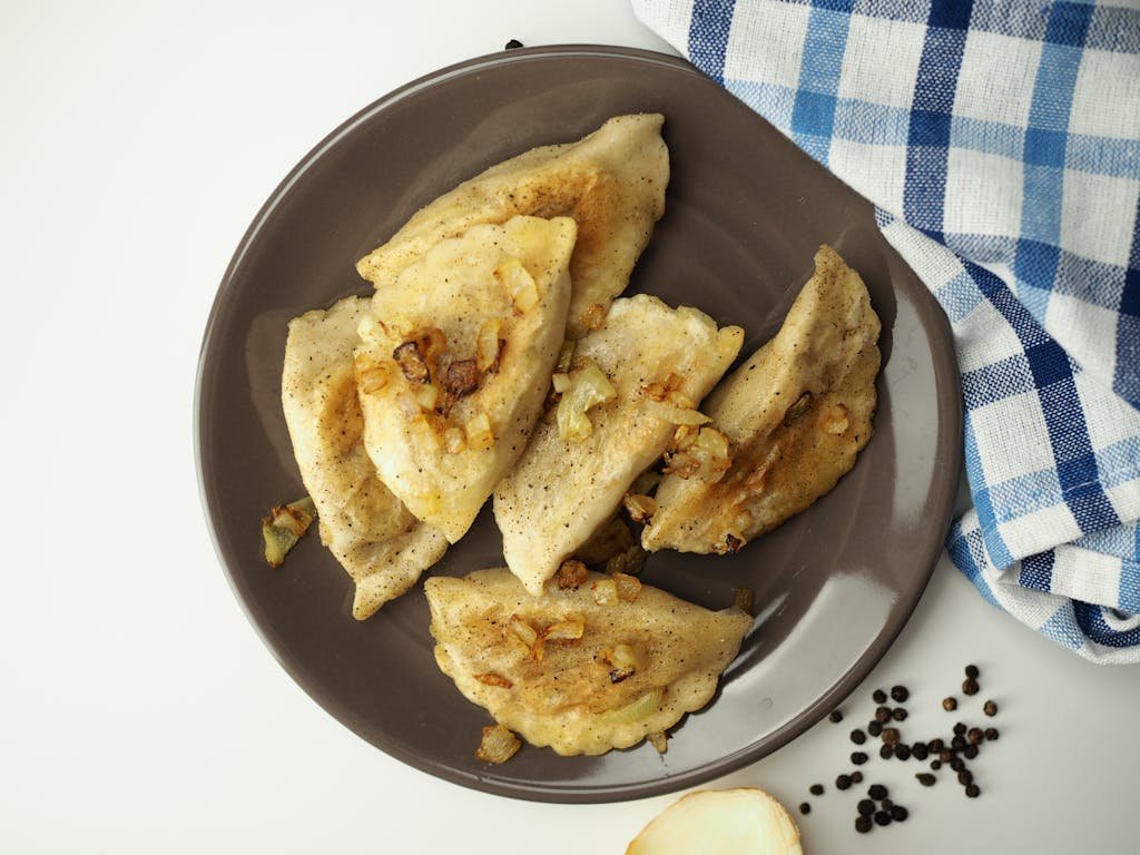 A tasty plate of homemade dumplings with fried onions on a table setting.