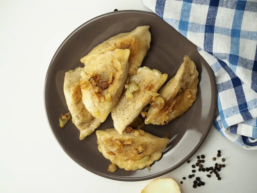 A tasty plate of homemade dumplings with fried onions on a table setting.