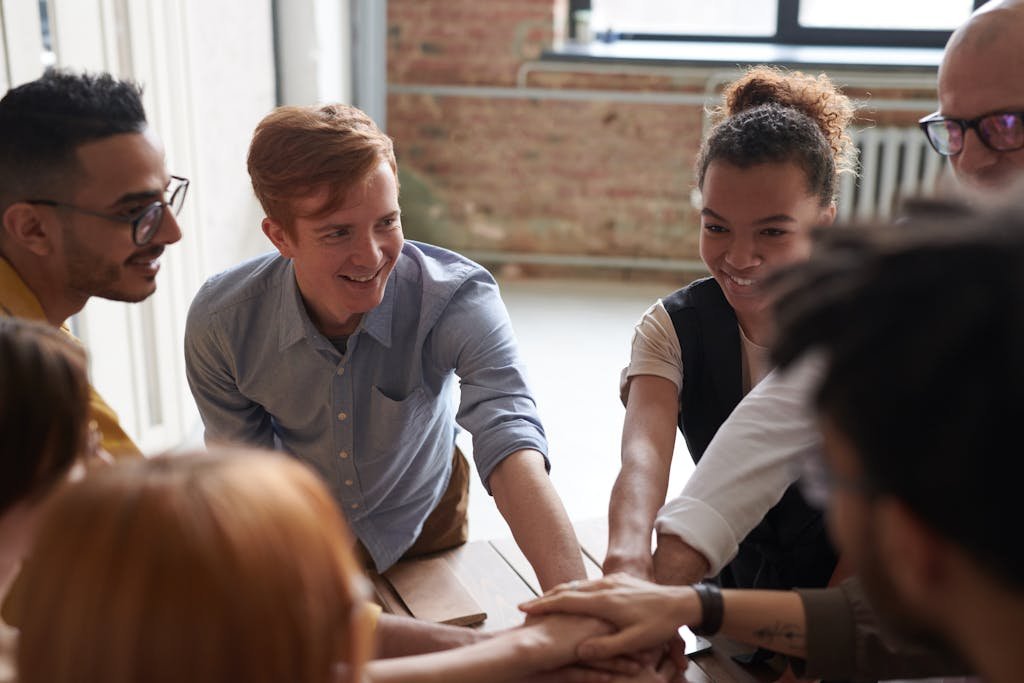 A diverse group of young professionals joining hands in a cheerful and supportive team-building activity.