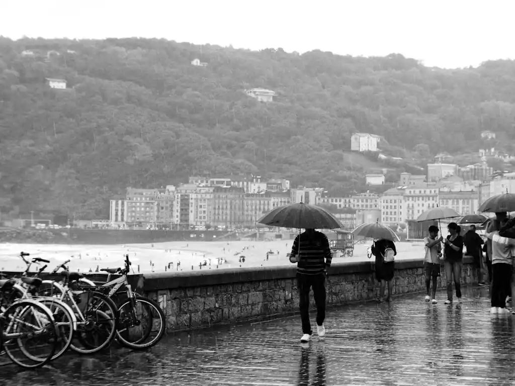 People walk with umbrellas on a rainy day along the beach in San Sebastián, Spain.